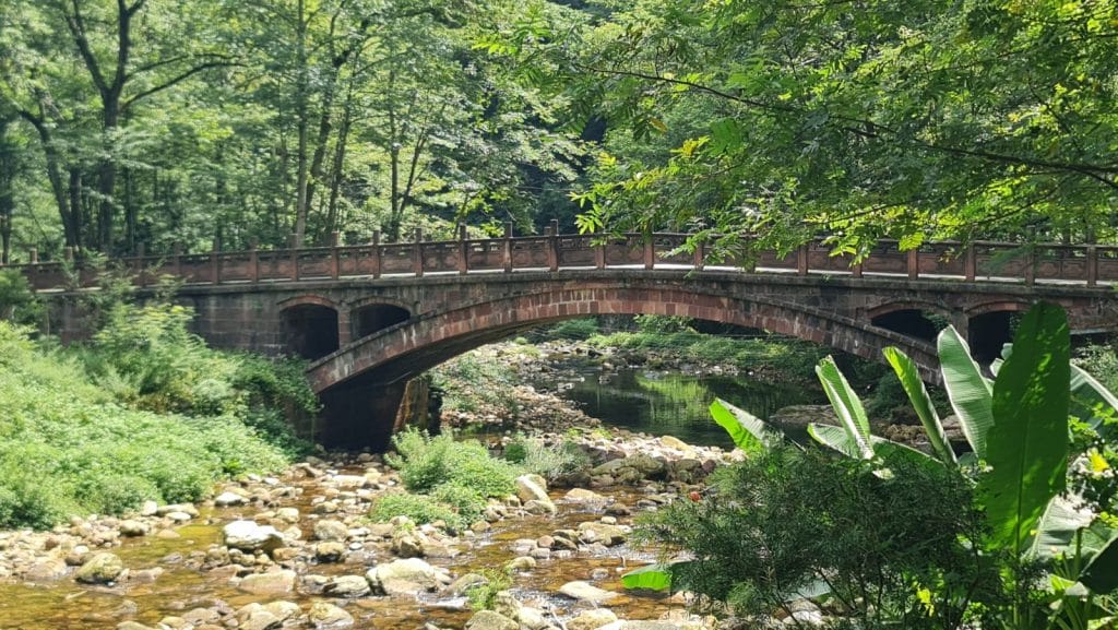 Steinbrücke über einen Bach in grüner Landschaft.