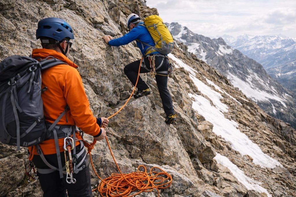 Bergsteiger klettern mit Seil auf felsigem Hang.