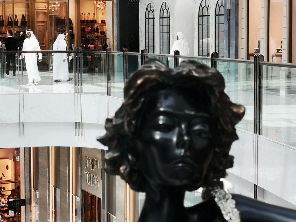 Skulptur vor Einkaufszentrum mit Passanten.