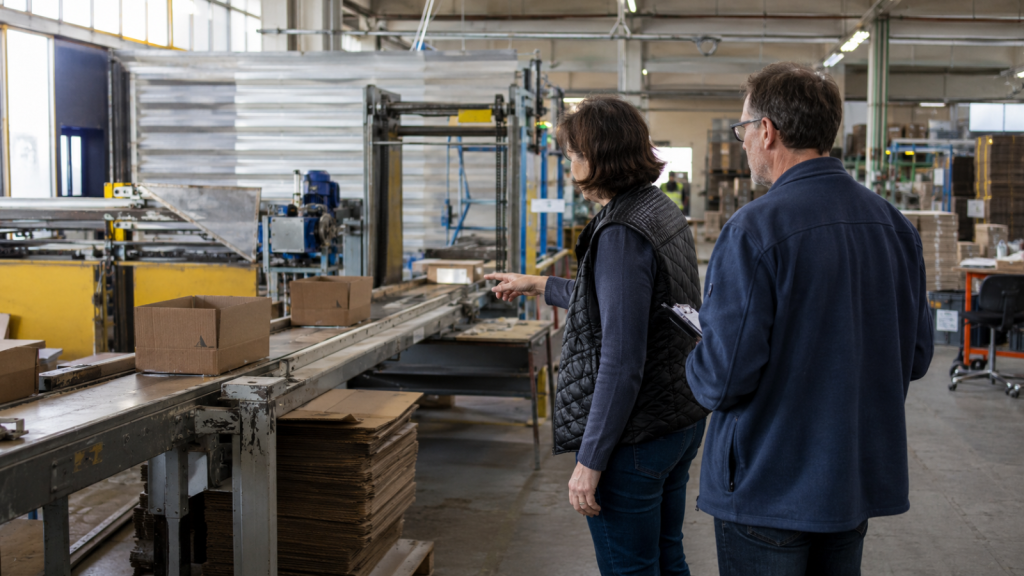 Zwei Mitarbeitende prüfen Kartonagen an einer Verpackungsmaschine