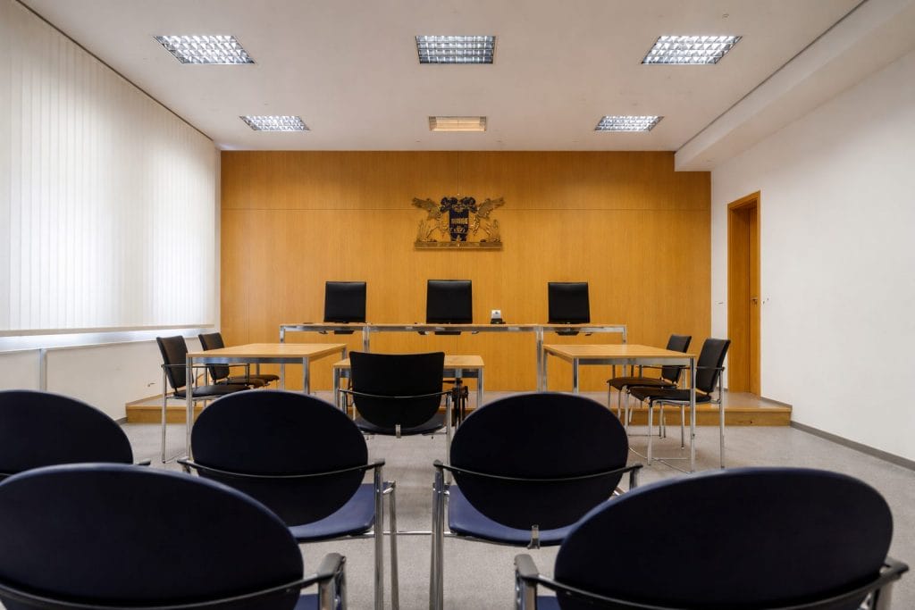 Leerer Gerichtssaal mit Stühlen und Richtertisch.